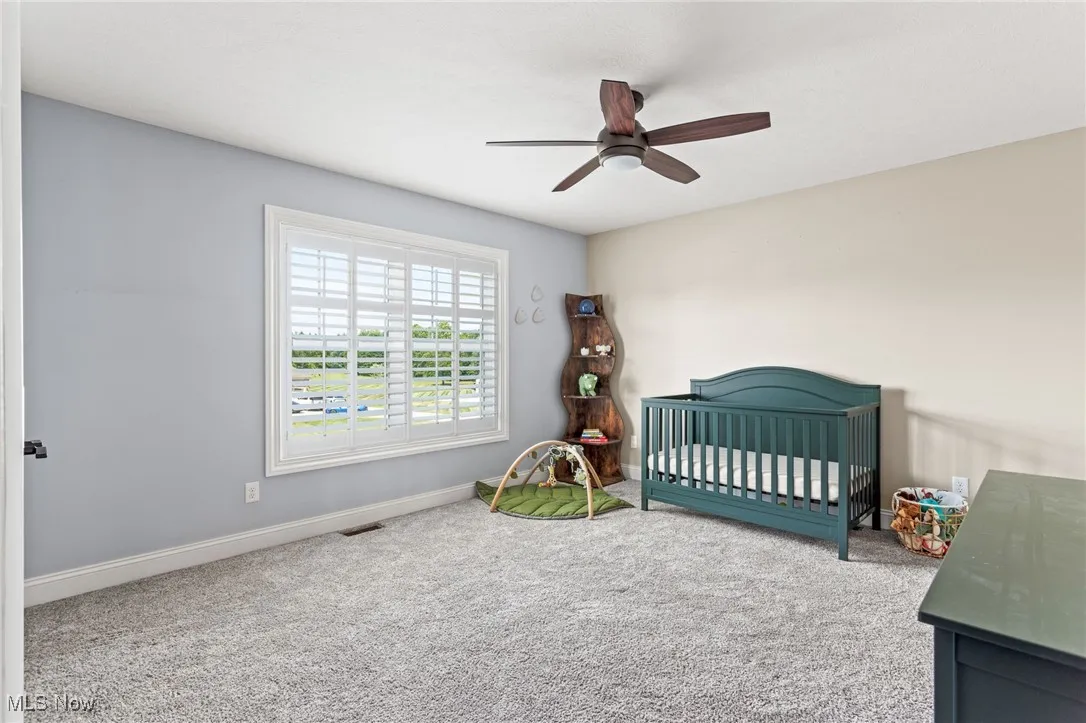 Carpeted bedroom with ceiling fan and a nursery area