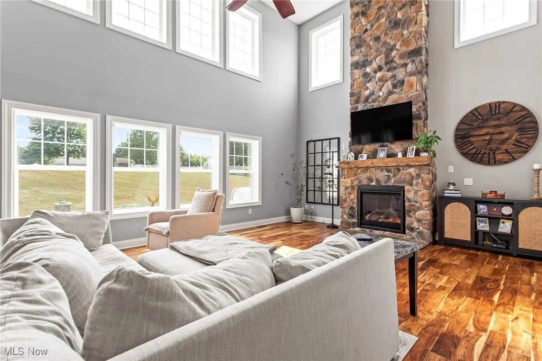 Living room with a high ceiling, a fireplace, ceiling fan, and wood finished floors