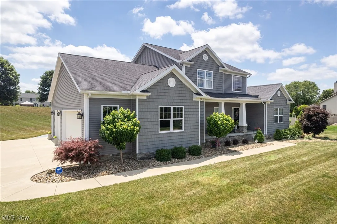 View of front of house with covered porch, driveway, a front yard, and roof with shingles