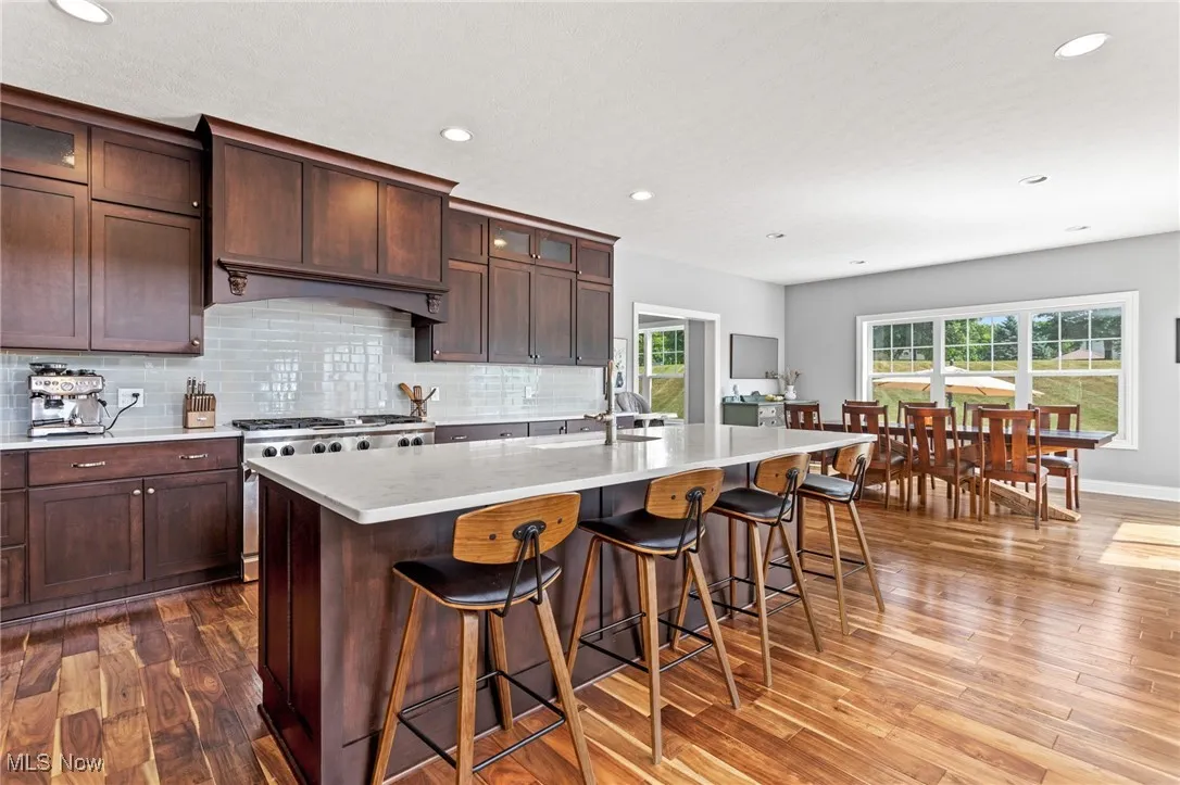 Kitchen featuring wood finished floors, light countertops, a kitchen breakfast bar, backsplash, and recessed lighting