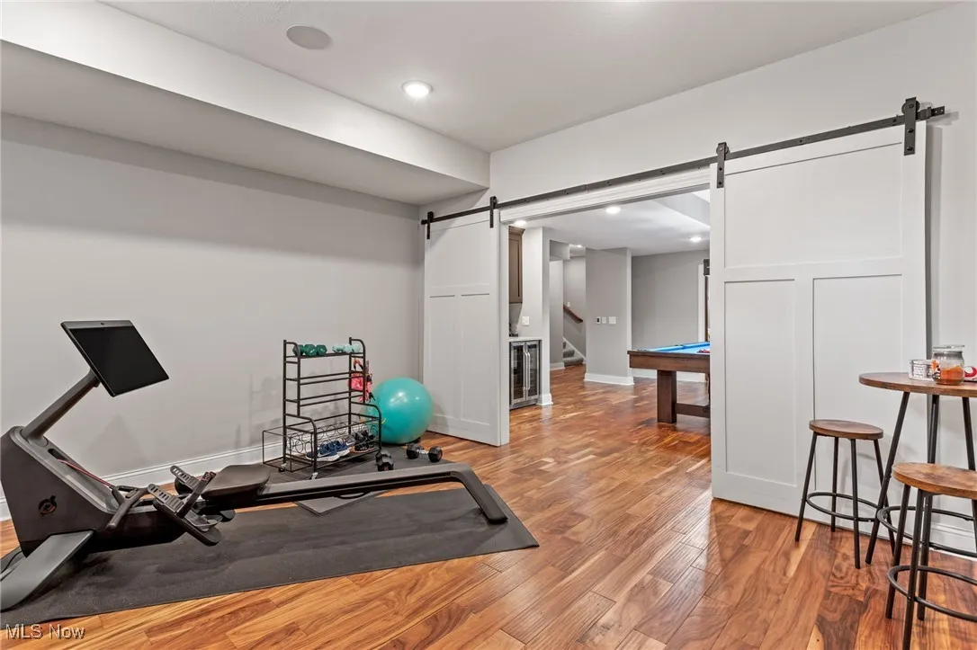 Exercise area with a barn door, wood finished floors, recessed lighting, and beverage cooler