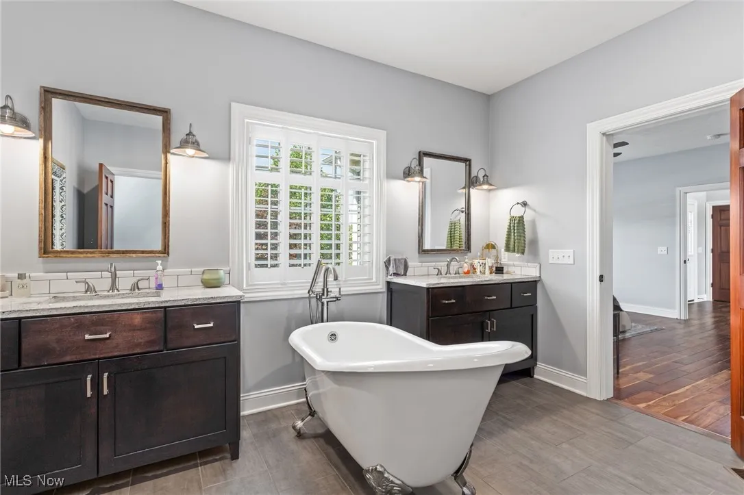 Bathroom featuring a freestanding bath, two vanities, and wood finished floors