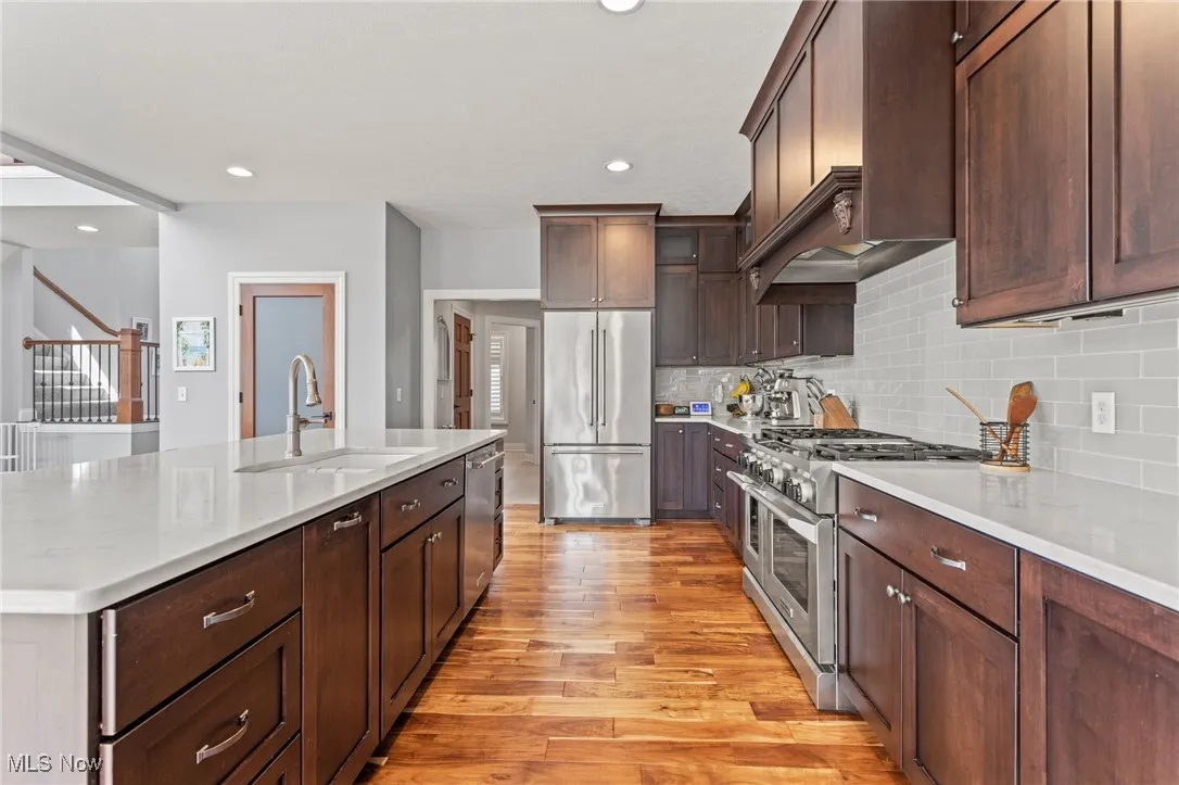 Kitchen featuring high end appliances, light wood-style flooring, decorative backsplash, an island with sink, and recessed lighting