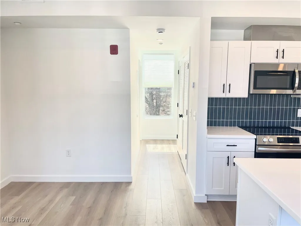 Kitchen with appliances with stainless steel finishes, light wood-type flooring, white cabinets, decorative backsplash, and light countertops
