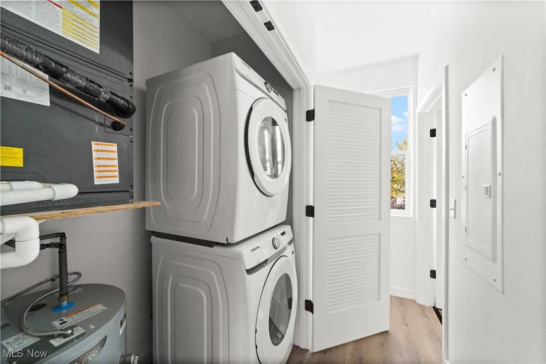 Laundry room featuring stacked washer / drying machine, heating unit, wood finished floors, electric panel, and water heater