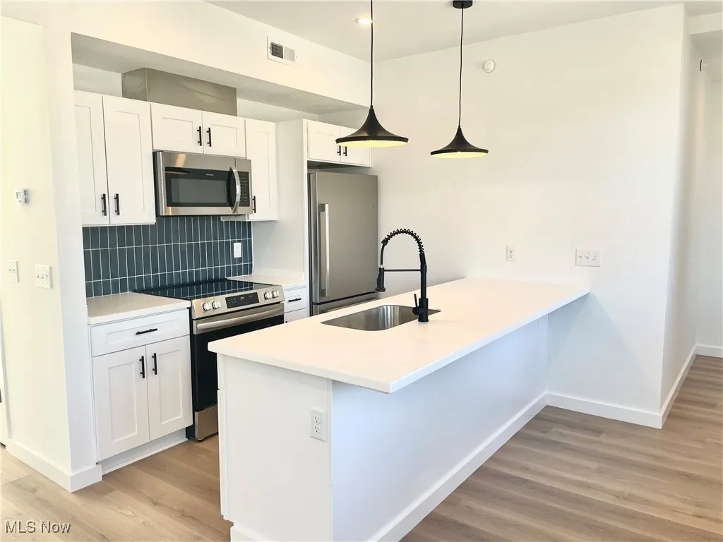 Kitchen featuring stainless steel appliances, light wood finished floors, a peninsula, tasteful backsplash, and white cabinetry