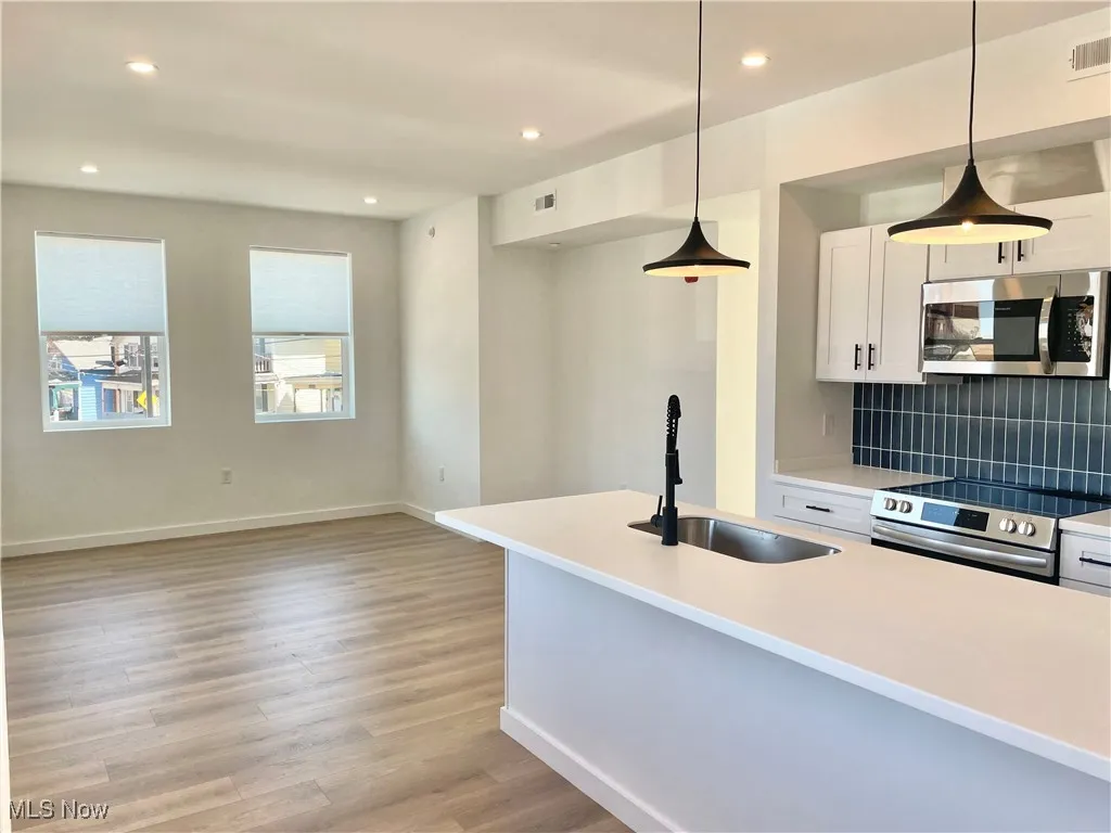 Kitchen with appliances with stainless steel finishes, backsplash, white cabinets, light wood-style flooring, and hanging light fixtures