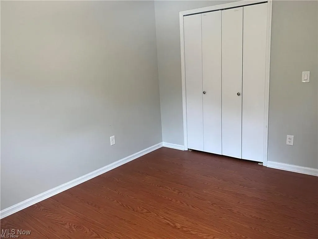 Unfurnished bedroom with dark wood-style floors and a closet