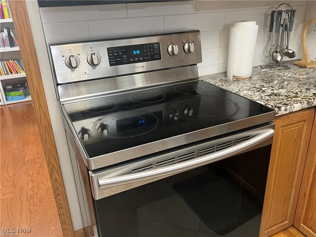 Kitchen view of stainless steel electric range, backsplash, brown cabinetry, and light stone counters