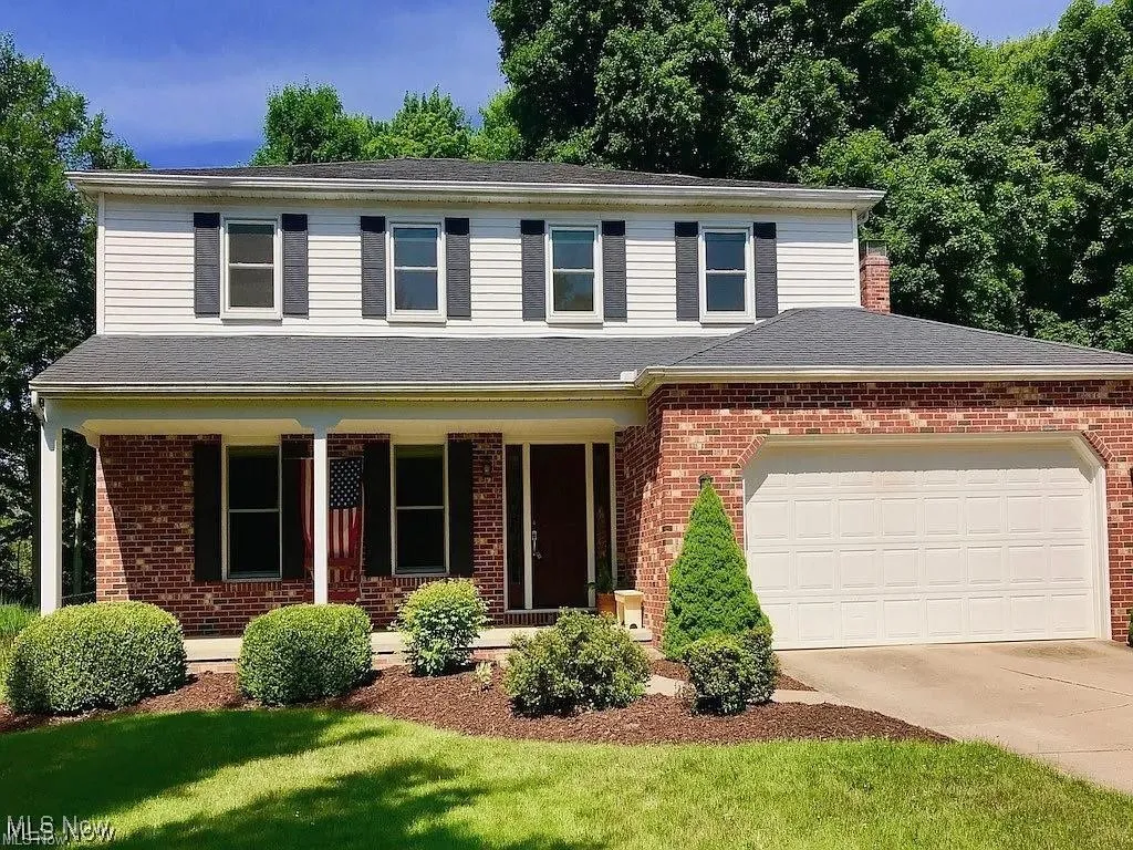 Traditional-style house with a porch, driveway, brick siding, an attached garage, and a shingled roof