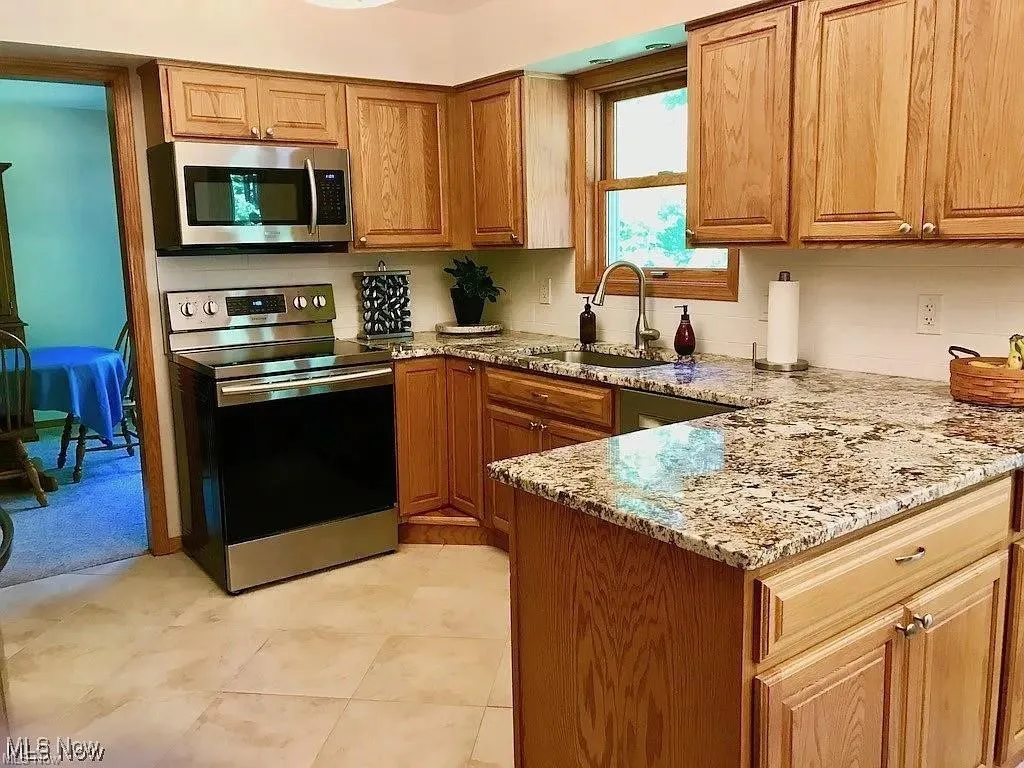 Kitchen with appliances with stainless steel finishes, light stone countertops, brown cabinets, and a peninsula