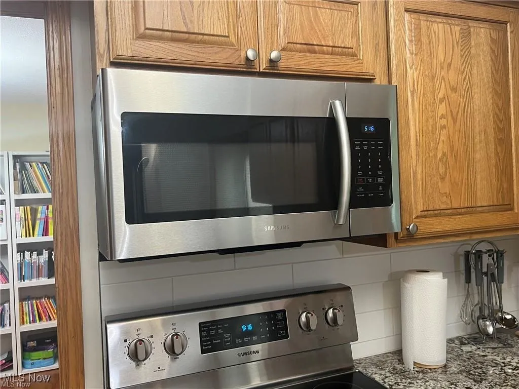 Kitchen view of stainless steel microwave, backsplash, stove, brown cabinetry, and mail area