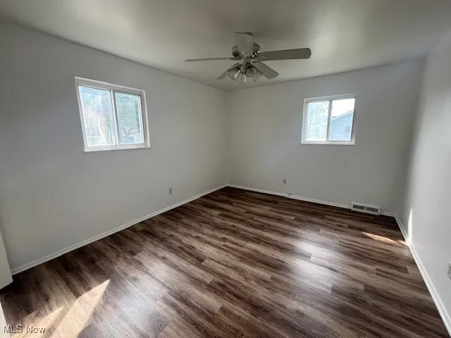 Empty room with a ceiling fan and dark wood finished floors