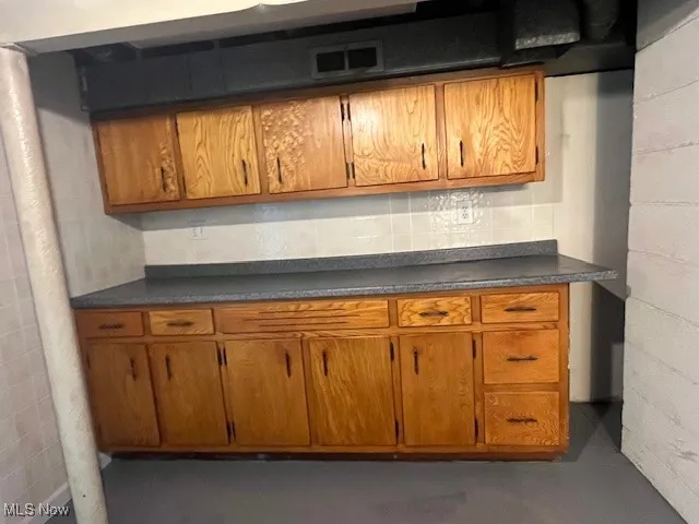 Kitchen with brown cabinets, dark countertops, finished concrete flooring, and concrete block wall
