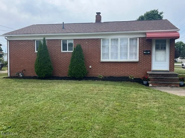 Single story home featuring a front yard, brick siding, a chimney, and entry steps