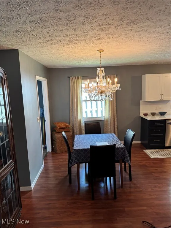 Dining area with a chandelier, dark wood-style floors, and a textured ceiling