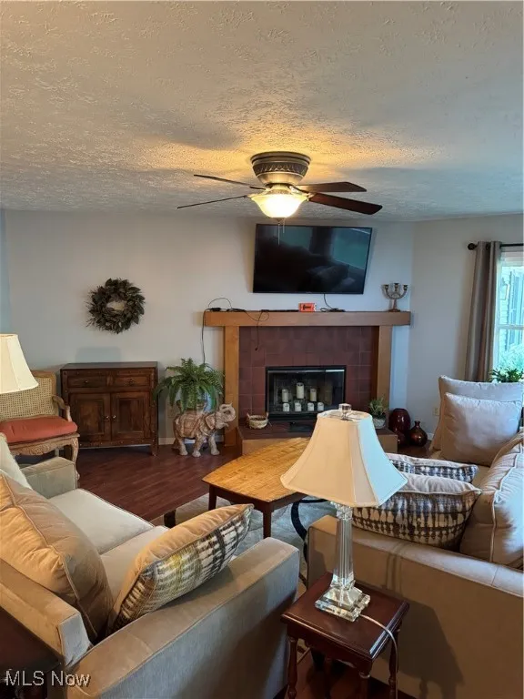 Living area with a textured ceiling, ceiling fan, wood finished floors, and a tile fireplace