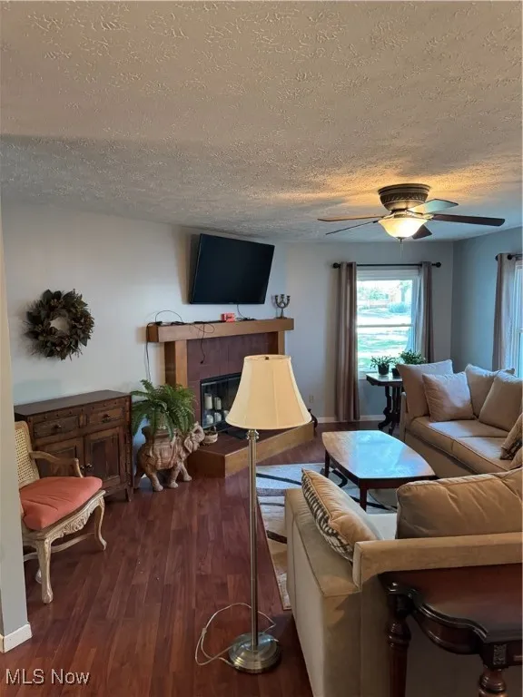 Living area featuring a textured ceiling, dark wood-type flooring, ceiling fan, and a fireplace