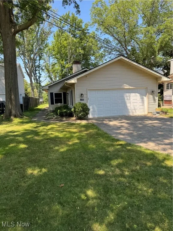 View of front facade featuring concrete driveway, a chimney, and a garage