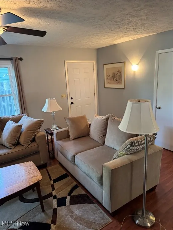 Living room with a ceiling fan, a textured ceiling, and wood finished floors