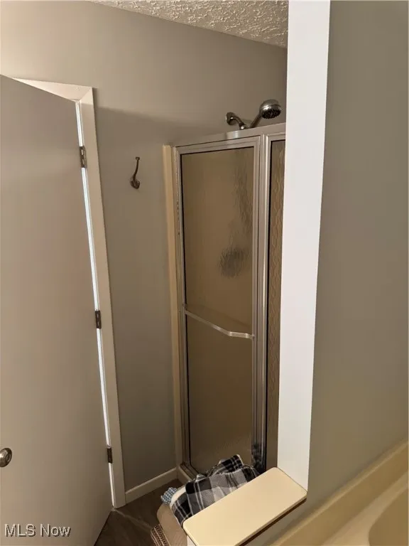 Full bathroom featuring a stall shower, a textured ceiling, and wood finished floors