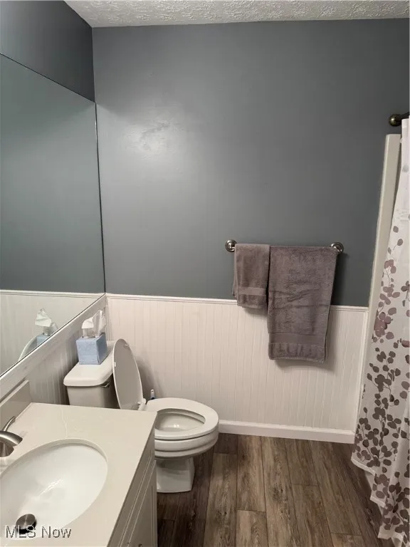 Full bath with a wainscoted wall, wood finished floors, vanity, and a textured ceiling