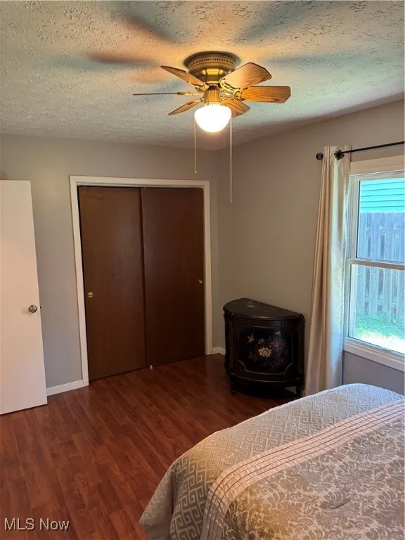 Bedroom with a wood stove, wood finished floors, a textured ceiling, a closet, and a ceiling fan
