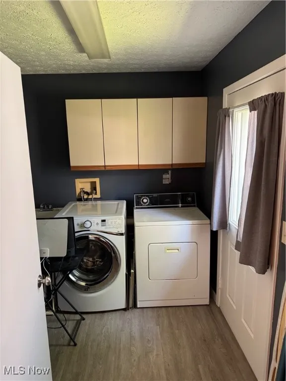 Washroom featuring wood finished floors, washer and dryer, cabinet space, and a textured ceiling