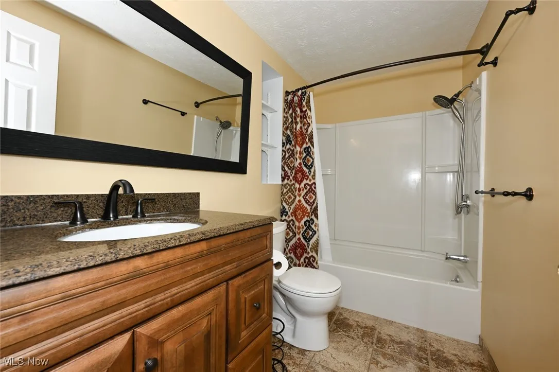 Bathroom featuring shower / bath combination with curtain, vanity, and a textured ceiling