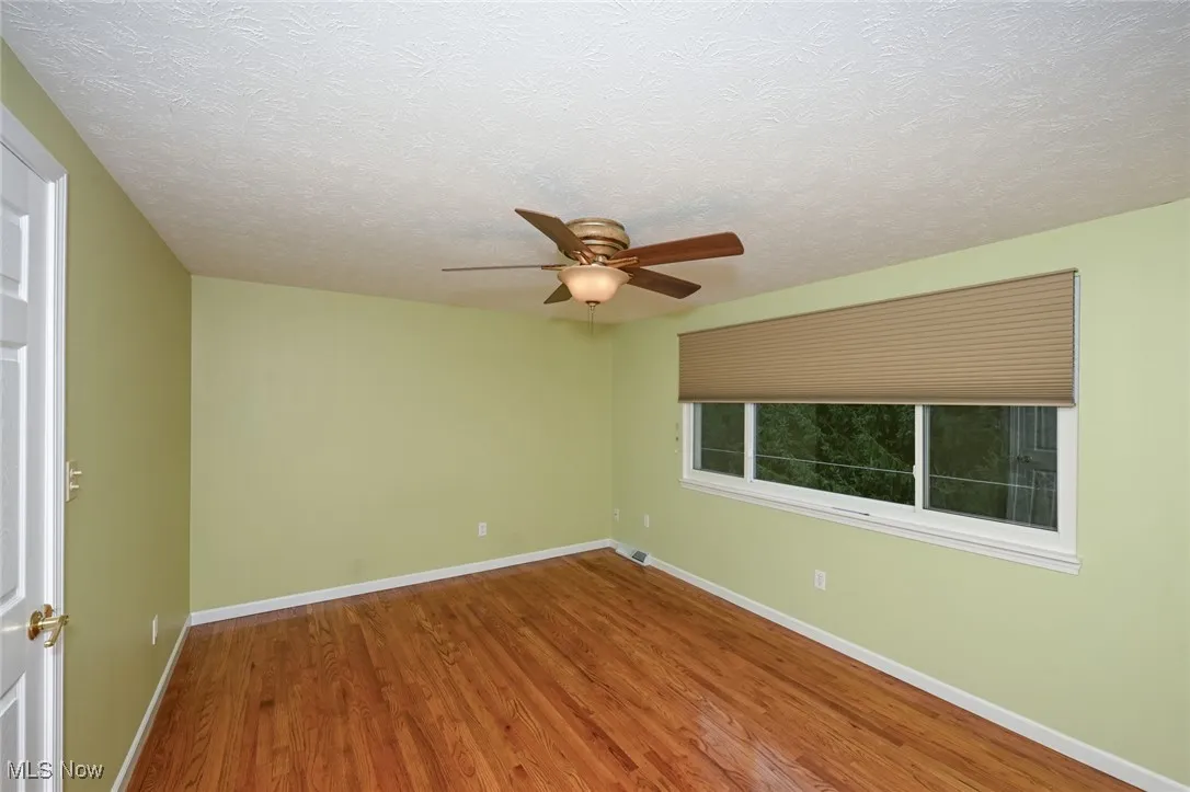 Unfurnished room featuring wood finished floors, ceiling fan, and a textured ceiling