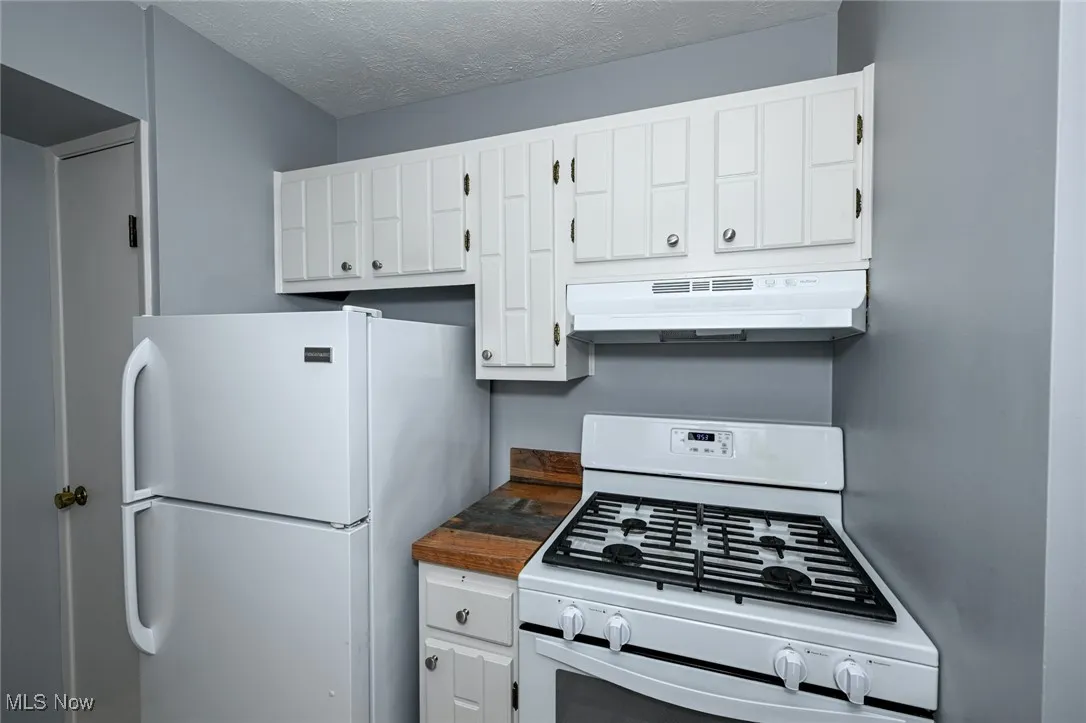 Kitchen with white appliances, under cabinet range hood, white cabinetry, dark countertops, and a textured ceiling