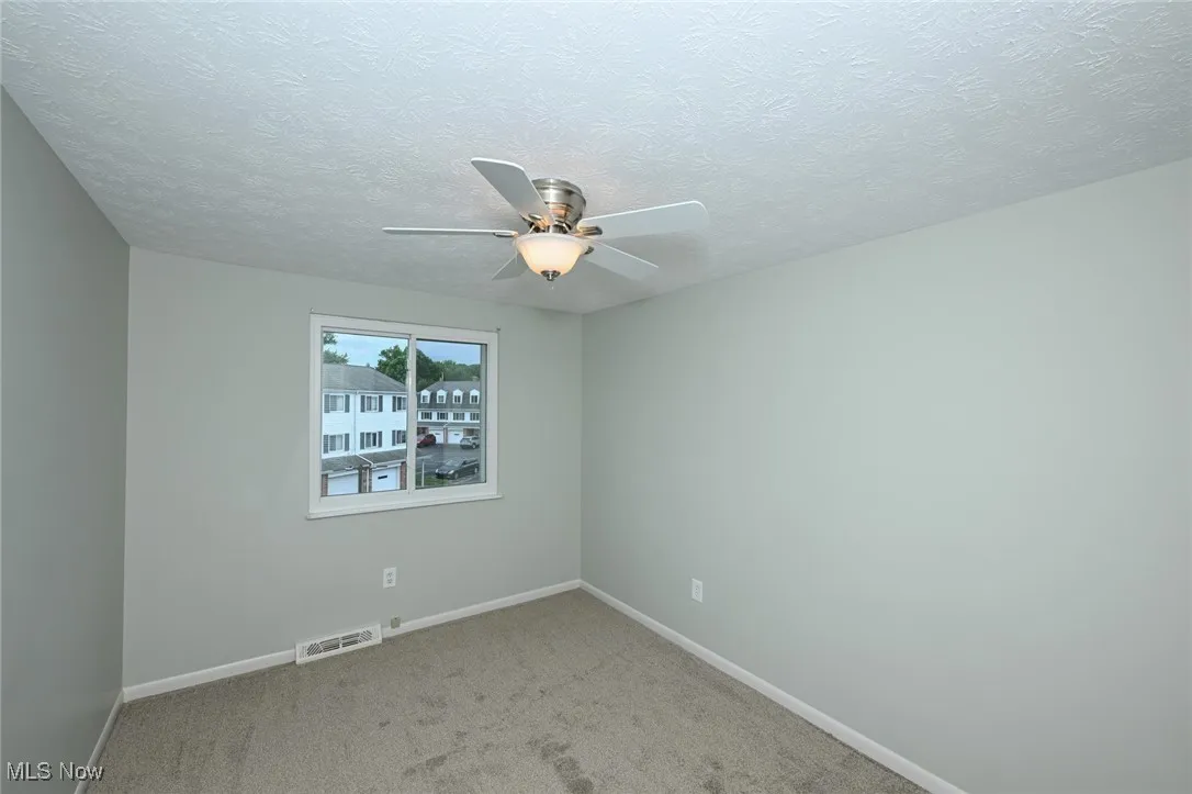 Empty room featuring a ceiling fan, carpet floors, and a textured ceiling