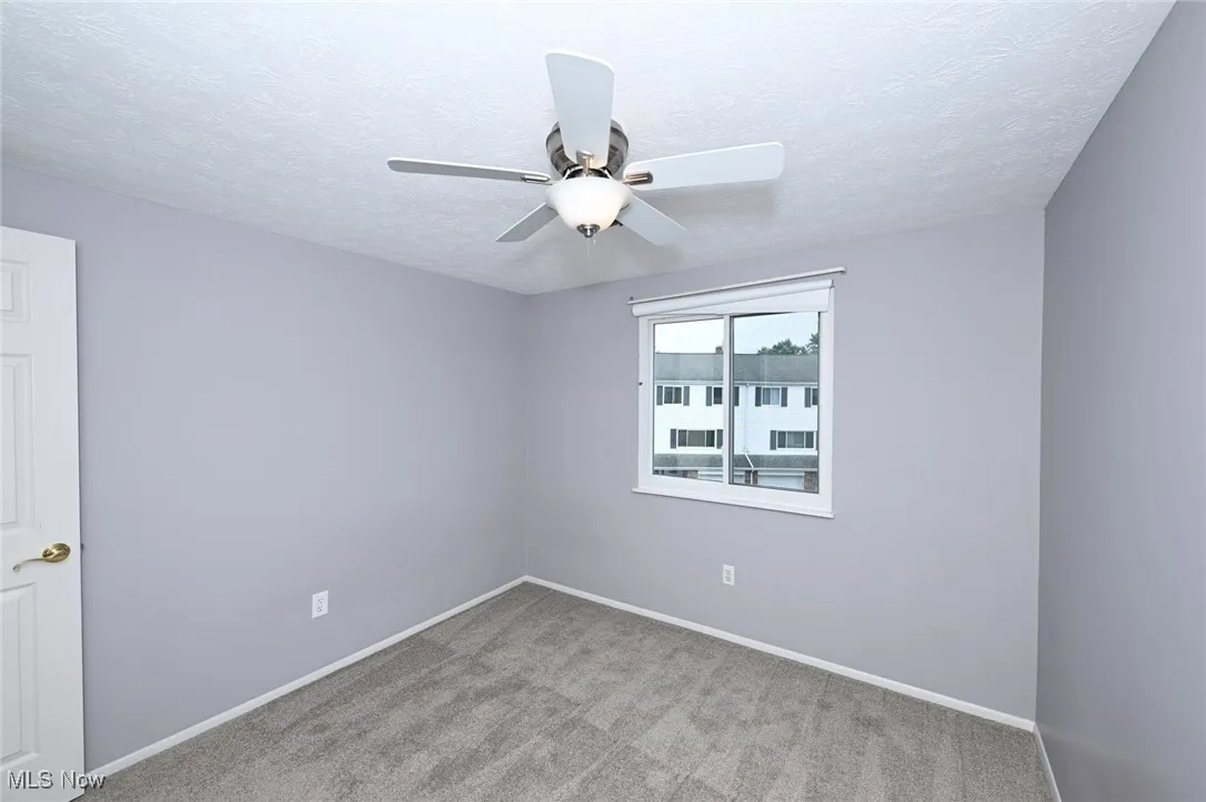 Carpeted empty room with ceiling fan and a textured ceiling