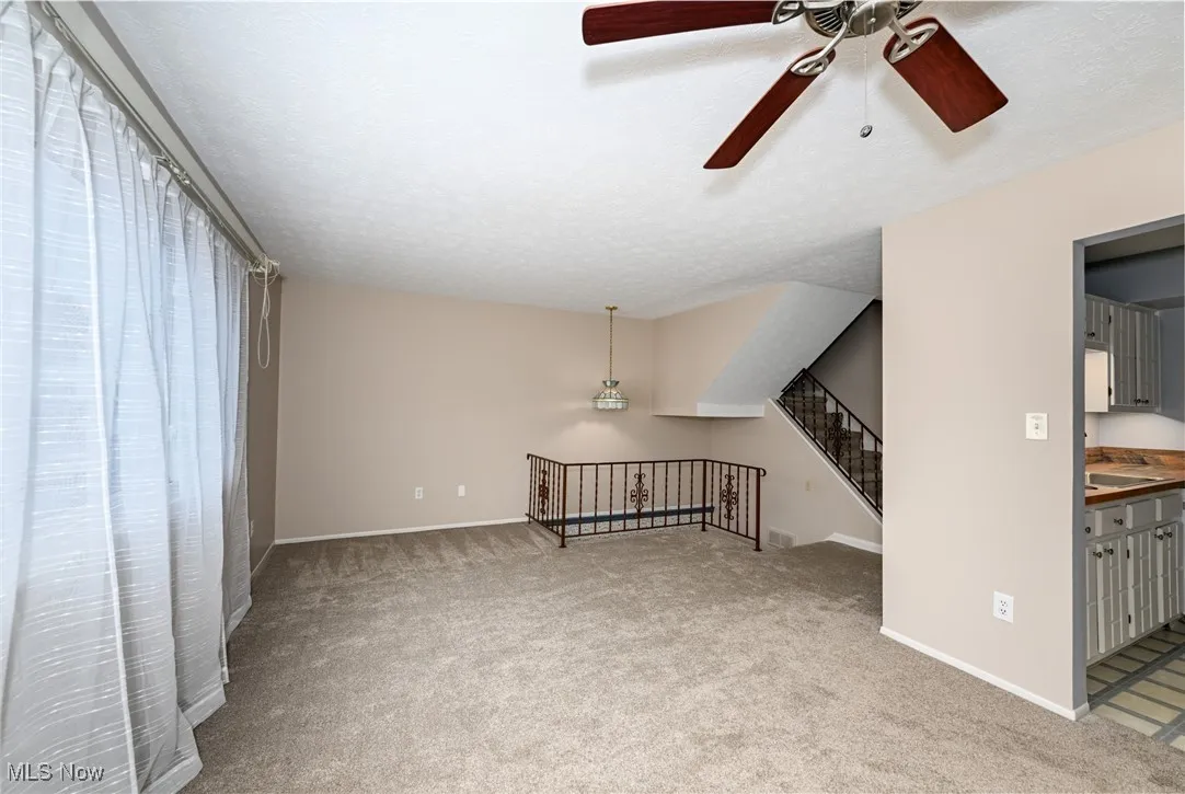 Unfurnished living room featuring a ceiling fan, carpet, and a textured ceiling