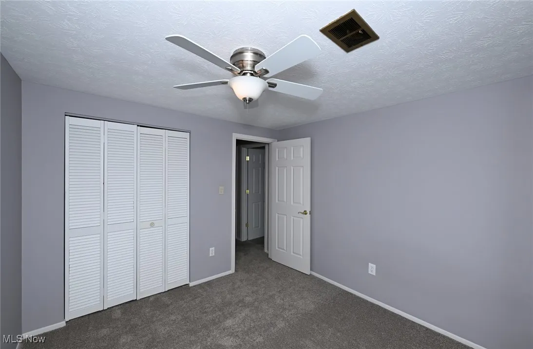 Unfurnished bedroom featuring a closet, dark colored carpet, ceiling fan, and a textured ceiling