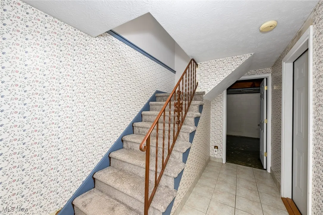 Staircase with wallpapered walls, a textured ceiling, and tile patterned flooring