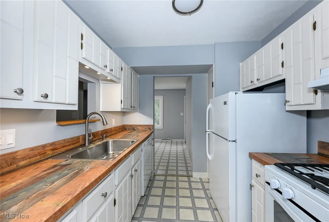 Kitchen featuring butcher block countertops, white cabinetry, and white appliances