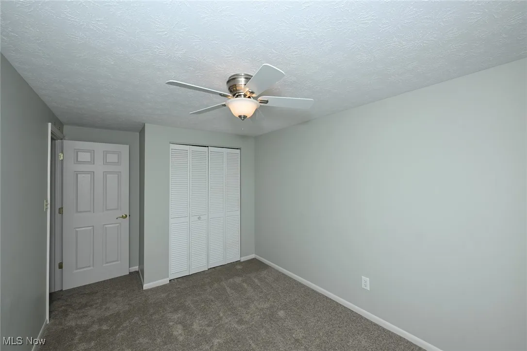 Unfurnished bedroom with a closet, dark carpet, a textured ceiling, and ceiling fan