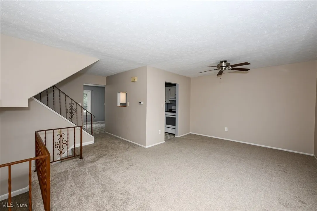 Unfurnished living room featuring ceiling fan, carpet flooring, stairway, and a textured ceiling