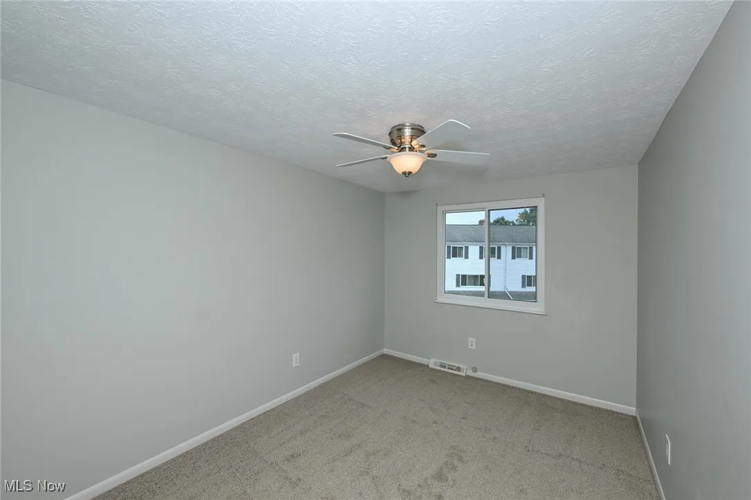 Empty room with ceiling fan, carpet floors, and a textured ceiling