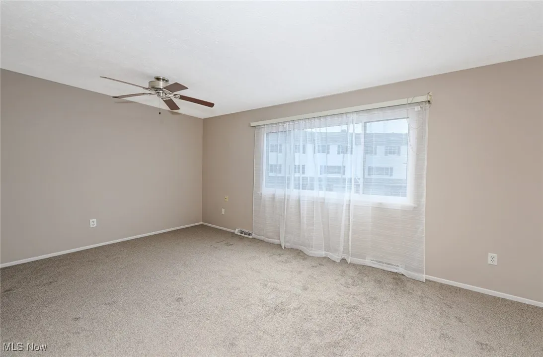 Carpeted empty room with ceiling fan and baseboards