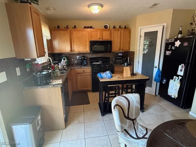 Kitchen with black appliances, decorative backsplash, and light tile patterned floors