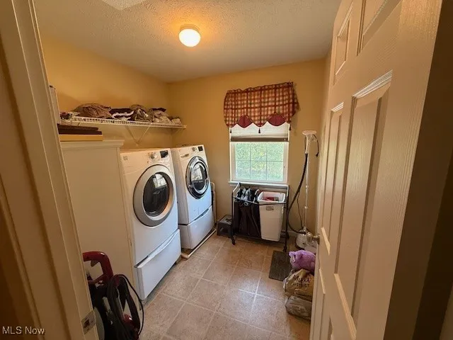 Laundry room with washing machine and clothes dryer, a textured ceiling, and light tile patterned floors