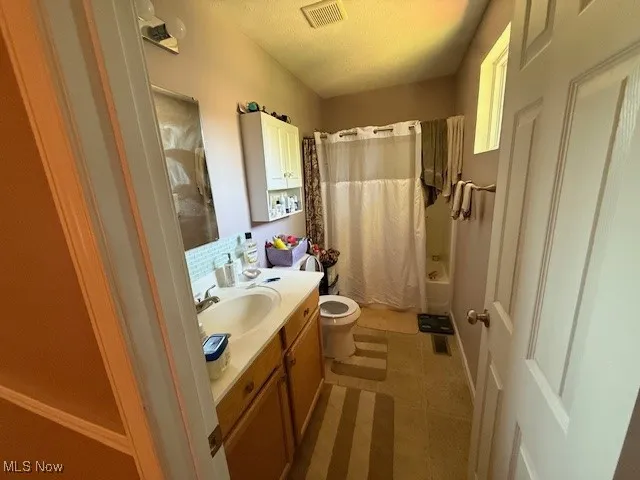 Bathroom featuring vanity, a textured ceiling, shower / bath combo with shower curtain, and tile patterned flooring