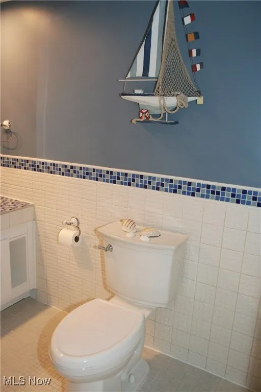 Half bathroom with tile walls, wainscoting, tile patterned flooring, and vanity