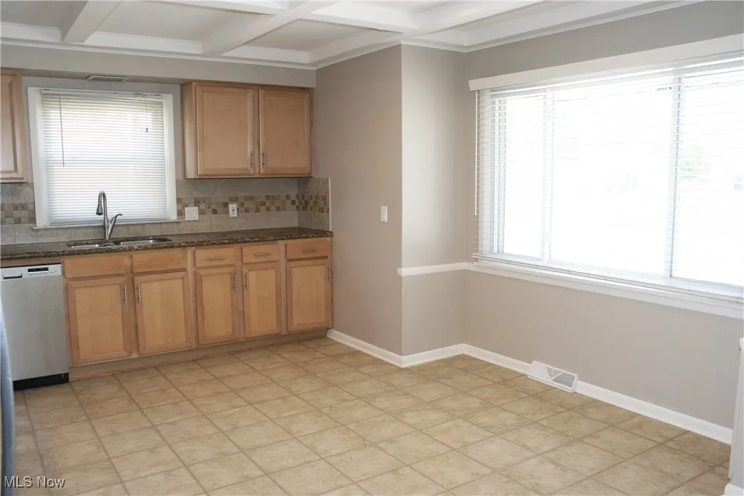 Kitchen featuring backsplash, beamed ceiling, dishwasher, coffered ceiling, and dark stone countertops