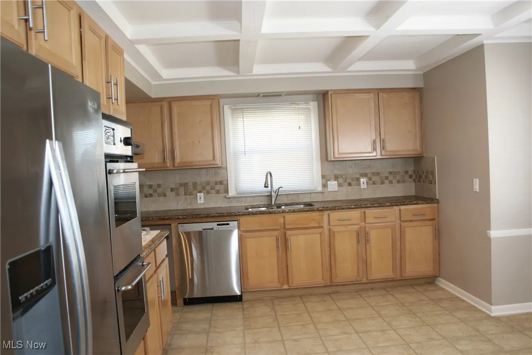 Kitchen with coffered ceiling, stainless steel appliances, tasteful backsplash, beamed ceiling, and dark stone countertops