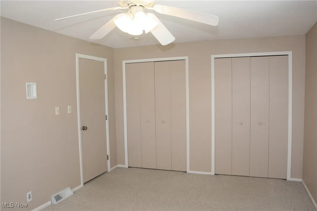 Unfurnished bedroom featuring two closets, light carpet, and ceiling fan