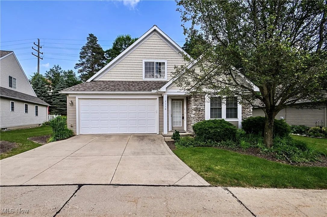 View of front facade with roof with shingles, driveway, stone siding, and a front yard
