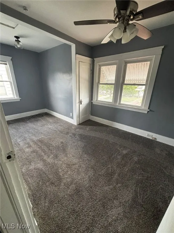 Spare room featuring ceiling fan, plenty of natural light, and dark colored carpet